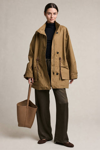 Woman wearing a brown coat and holding a matching bag against a neutral background