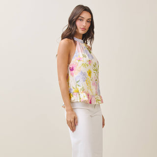 Woman wearing a floral sleeveless top and white pants on a plain background