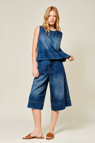 Woman wearing a denim outfit with a sleeveless top and wide-leg pants on a beige background