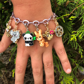 Hand wearing a colorful charm bracelet with various animal charms against a green leafy background
