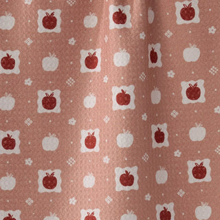 A close-up of a fabric or wallpaper pattern featuring red apples and white pumpkins on a dusty terracotta background.