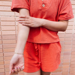Person wearing an orange shirt and shorts against a tiled wall.
