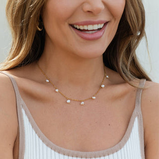 Woman wearing a gold necklace with pearl drops against a neutral background