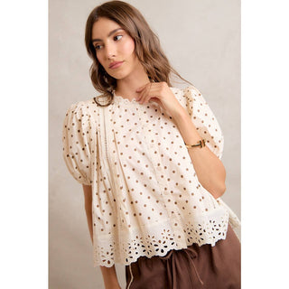Woman wearing a cream blouse with lace details against a neutral background