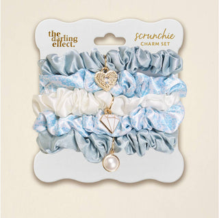 Set of scrunchies with charms on a branded card, displayed against a beige background.