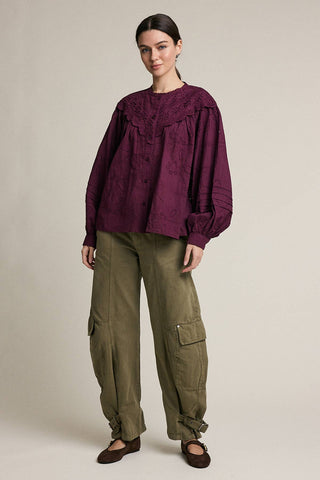 Woman wearing a purple blouse and green cargo pants on a beige background