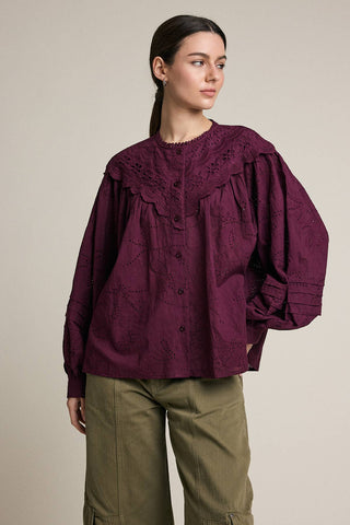 Woman wearing a burgundy blouse with puffed sleeves and green pants on a beige background