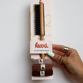 Hand holding a hairbrush with packaging labeled 'kaxi' on a white background