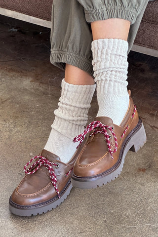 Brown shoes with red laces worn with white socks on a concrete floor.