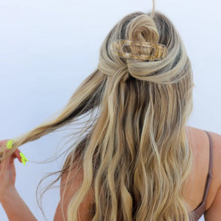 Person with long, wavy hair wearing a gold headband against a light blue background