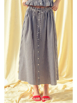 Person wearing a black and white checkered dress with red sandals on a yellow background
