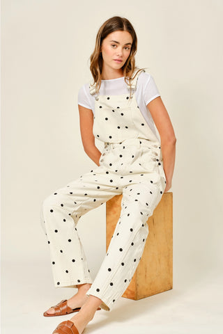 Woman wearing a polka dot jumpsuit sitting on a wooden block against a plain background