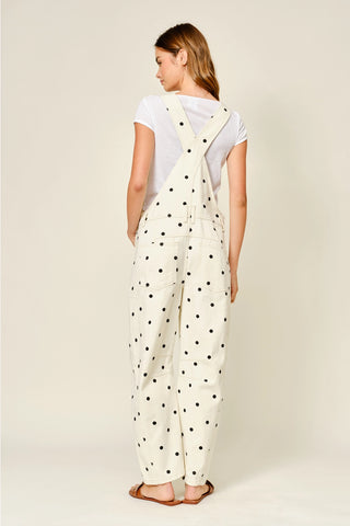 Woman wearing a white polka dot jumpsuit on a plain background
