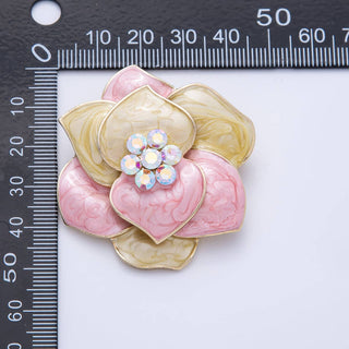 Pink and gold flower-shaped brooch with a central gemstone on a white background with a ruler for scale.