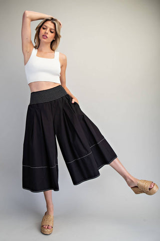 Woman wearing a white top and black wide-leg pants on a plain background