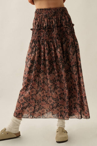 A tiered, high-waisted maxi skirt with a dark brown and dusty rose floral print, styled with white socks and beige flat shoes against a plain light beige background.