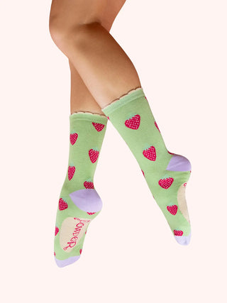 Green socks with red hearts worn by a person on a white background