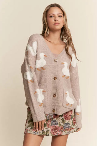 Woman wearing a beige cardigan with white duck patterns and a floral skirt on a beige background