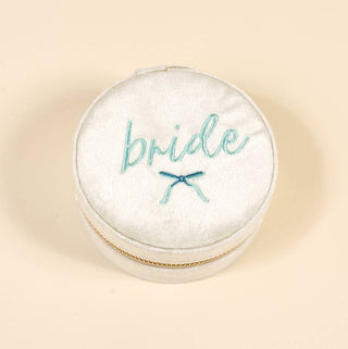 Round white jewelry box with 'bride' embroidered on it against a beige background