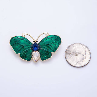 Green butterfly brooch with gemstones next to a quarter on a white background