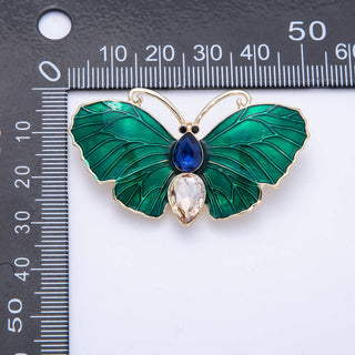Green butterfly-shaped brooch with gemstones on a ruler for scale