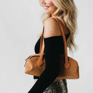 Woman holding a brown handbag against a plain background