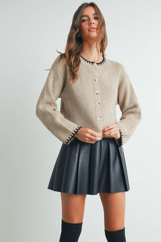 Woman wearing a beige knitted cardigan and black pleated skirt on a white background