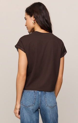 Woman wearing a brown t-shirt and blue jeans against a beige background