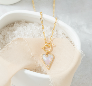 Gold necklace with a heart-shaped pendant on a white stone surface