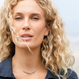 Woman with curly blonde hair wearing gold hoop earrings and a necklace against a light background