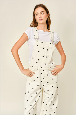 Woman wearing a white polka dot jumpsuit over a white t-shirt on a beige background
