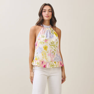 Woman wearing a floral halter top and white pants on a plain background