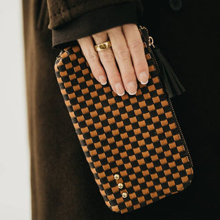 Hand holding a brown and black checkered clutch bag with a blurred background