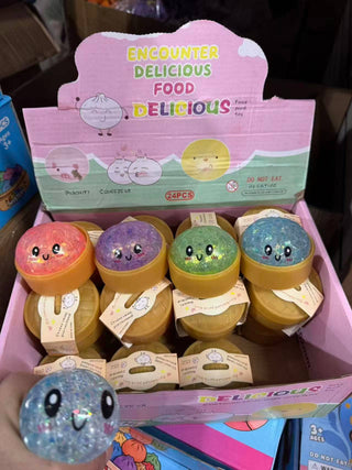 Box of small containers with cute faces and a colorful box labeled 'Encounter Delicious Food Delicious' on a dark background.