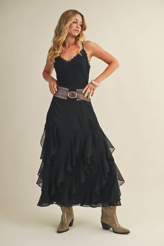 Woman wearing a black dress with ruffled layers and brown boots on a beige background