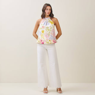 Woman wearing a floral top and white pants on a plain background