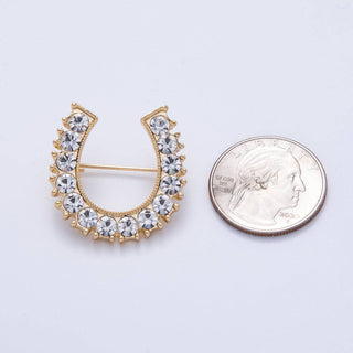 Gold brooch with crystal stones next to a quarter for scale on a light gray background