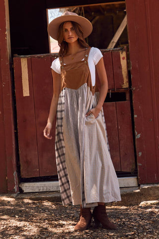 Woman in a plaid dress and wide-brimmed hat standing in front of a red wooden door.