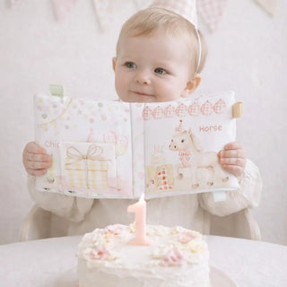 Baby holding a book with a birthday cake and lit candle in the foreground
