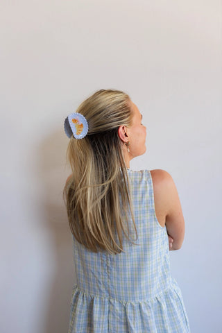 Woman with a hair clip wearing a blue checkered dress against a white background