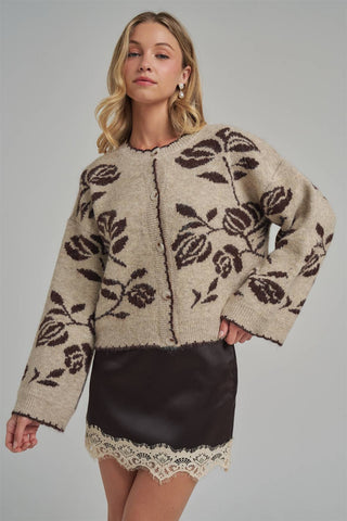 Woman wearing a beige cardigan with black floral patterns on a gray background
