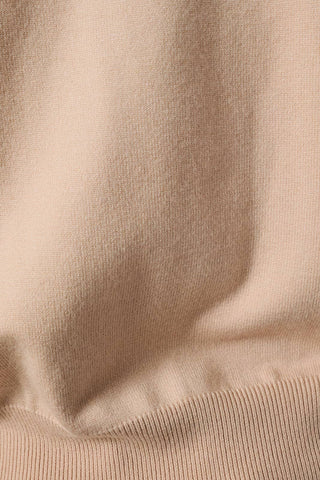 Close-up of a soft knit fabric in a warm light beige or cream tone, showing the texture and ribbed hem.
