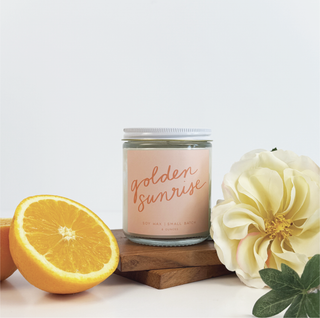 Candle labeled 'golden sunrise' with an orange and flower on a light background