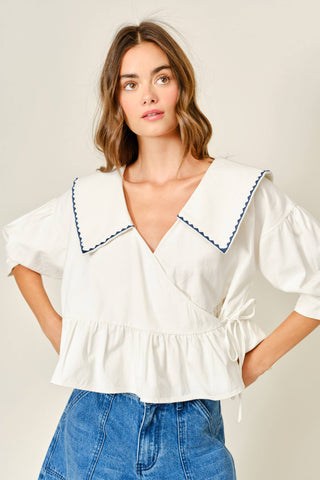 Woman wearing a white blouse with blue trim and blue jeans on a plain background