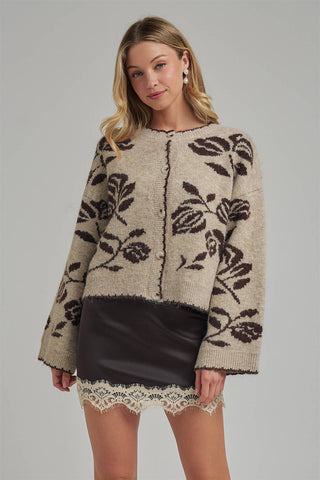 Woman wearing a beige sweater with black floral patterns and a black skirt on a gray background