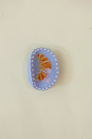 Decorative hair clip with a croissant design on a beige background