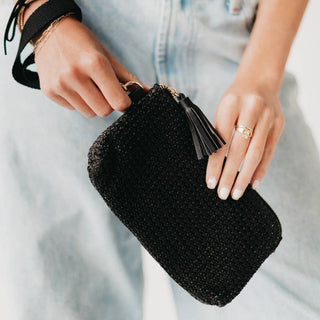 Black beaded clutch held by a person with a blurred light blue background