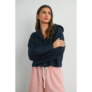 Woman wearing a navy blue sweater over a pink striped dress against a plain background