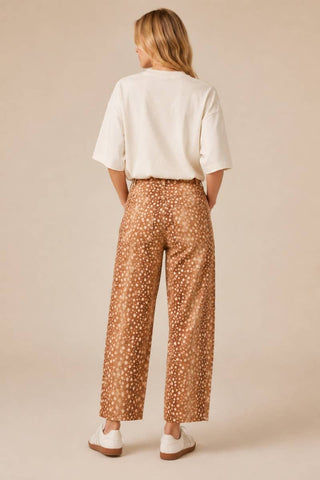 Woman wearing a white top and patterned brown pants against a beige background