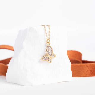 Gold butterfly necklace on a white cushion with a brown border